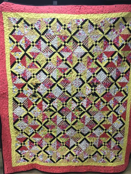 A bright and busy quilt with a complex geometric pattern in yellow, red, and black.