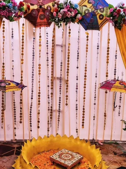 A creative Haldi setup using hanging Rajasthani umbrellas and strings of gota patti discs. The golden urli in the center is ready for the ceremony, surrounded by a warm, shimmering backdrop.