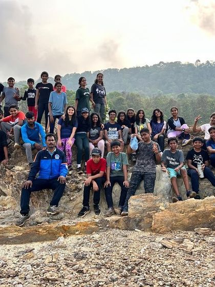 The entire group, along with instructors, poses for a photo on the rocky terrain overlooking the water at Dandeli.
