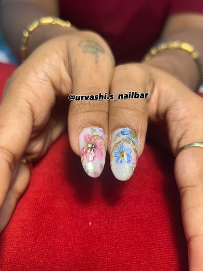 A royal garden on your fingertips. This design combines hand-painted pastel flowers with elegant gold chain details over a mix of mauve and pearly white nails.