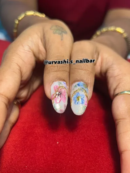 A royal garden on your fingertips. This design combines hand-painted pastel flowers with elegant gold chain details over a mix of mauve and pearly white nails.