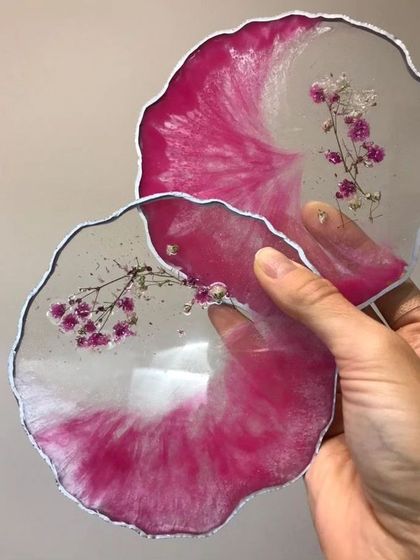 These geode-style resin coasters feature a striking pink and white swirl design with delicate sprigs of baby's breath preserved within the clear resin.