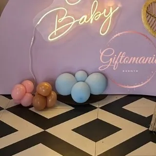 A simple yet chic setup with a 'Baby' neon sign against a lavender wall, with small balloon clusters indicating a gender reveal theme.