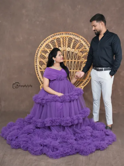 A regal studio portrait of a couple, with the mother-to-be seated on a peacock chair in a purple ruffled gown.