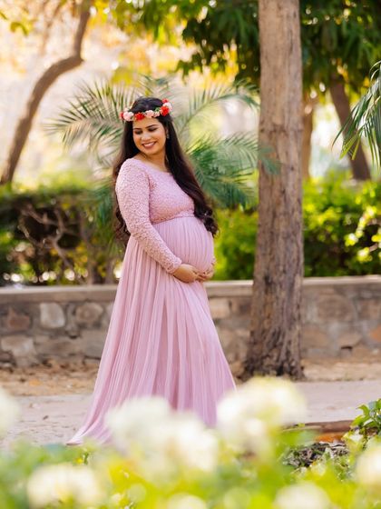 A mother-to-be wearing a floral crown walks through a sunlit park. The soft focus on the foreground flowers adds a dreamy quality to this beautiful outdoor maternity portrait.