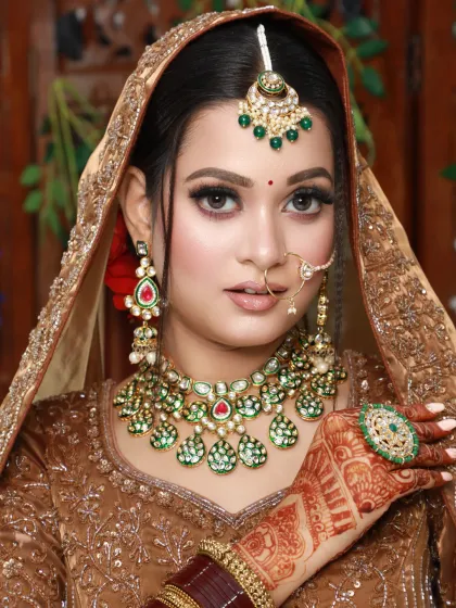 A classic portrait of a bride in a bronze lehenga, showing off her beautiful green jewelry and matching makeup details.