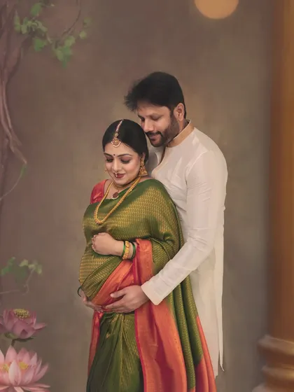 A perfect, timeless portrait capturing the deep connection between a couple. The rich green and orange Kanchivaram saree and traditional jewelry are complemented by the soft, painterly backdrop, creating a frame filled with elegance.