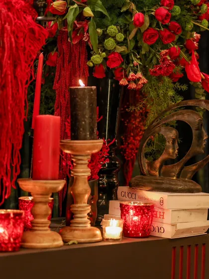 A close-up of the rich textures and deep red tones, where candles, art pieces, and books are layered to create a visually interesting and sophisticated decor moment.