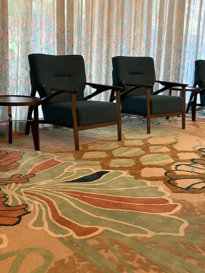 A close-up of the seating area in the GCC Hotel, showing the contrast between the dark wood of the chairs and the vibrant, large-scale pattern of the hand-tufted carpet.