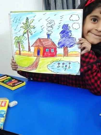 A young artist proudly presents her colorful landscape drawing, complete with a house, pond, and palm trees. Our classes help children build the skills to bring their imaginative scenes to life.