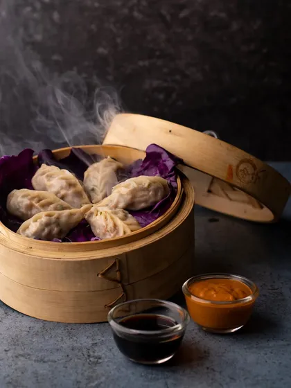 Steamed momos served in a traditional bamboo steamer. The steam rising from the basket adds a touch of authenticity and makes the momos look fresh and hot.
