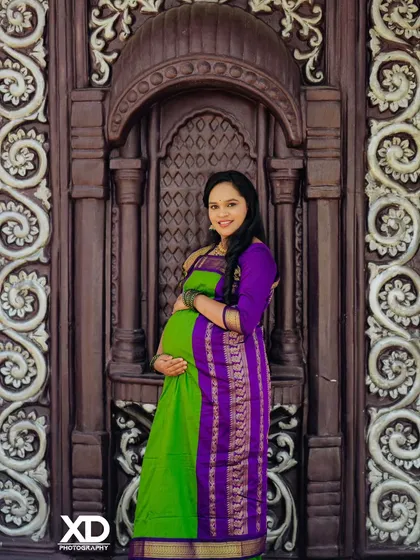 A beautiful solo portrait of the mother-to-be in a green and purple saree, framed by an ornate doorway.