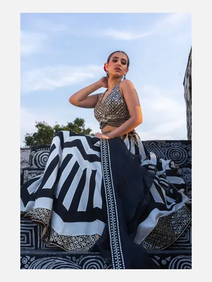 A model seated on a patterned staircase, wearing a contemporary black and white lehenga with a sequined blouse against a clear blue sky. This shot showcases modern ethnic wear in a unique, artistic location.