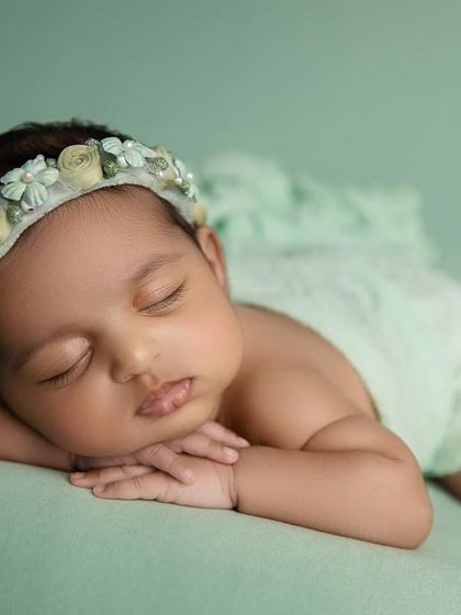 A classic 'chin on hands' pose on a mint green backdrop. The floral headband adds a delicate, natural touch.