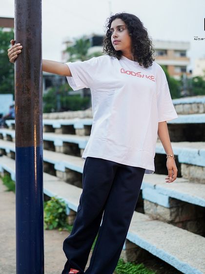 The Godsake graphic tee in an urban setting. Its clean white color and oversized fit make it a versatile piece for any streetwear enthusiast.