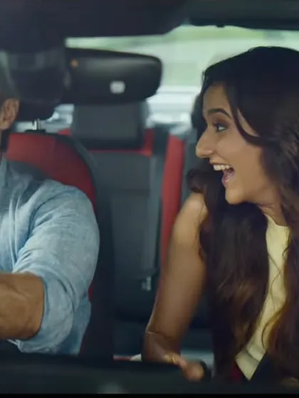 A fun, energetic shot from inside the car. The woman's bright yellow top and the man's casual blue shirt create a vibrant, happy mood for their road trip.