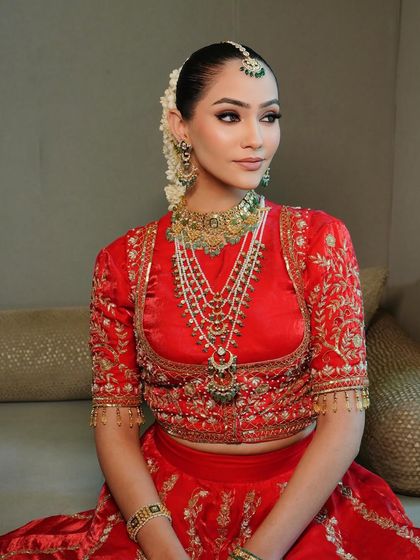 A classic red bridal lehenga, rich in color and tradition. This look features a beautifully embroidered blouse and layered pearl and emerald jewelry, perfect for the main wedding ceremony.