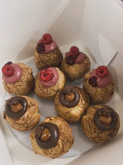 A box of assorted choux pastries, with raspberry and chocolate caramel flavors, ready for a Mother's Day gift.