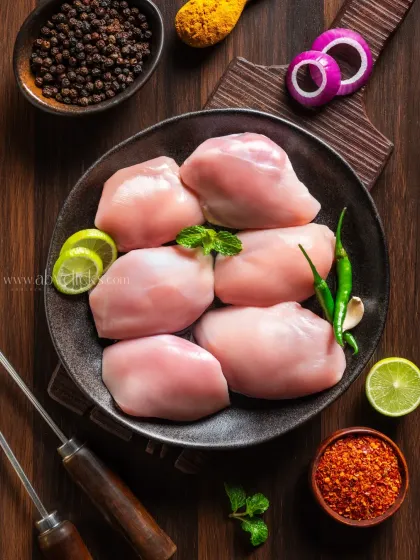 Boneless chicken thighs in a bowl, styled with mint, lime, and various spices for a flavorful presentation.