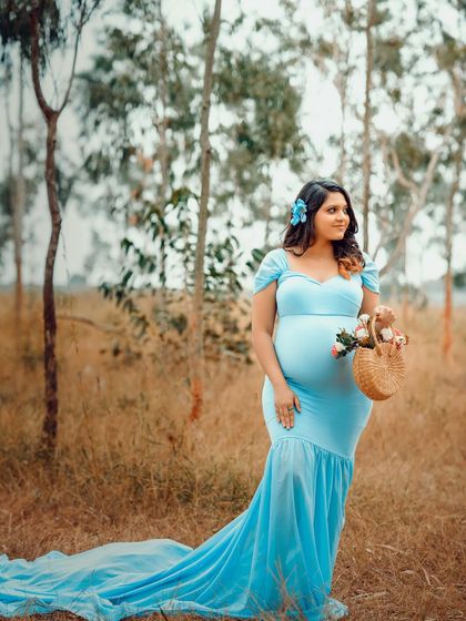 A simple and beautiful portrait of a mom-to-be in a blue gown, holding a basket of flowers. The rustic background adds to the charm of the photo.