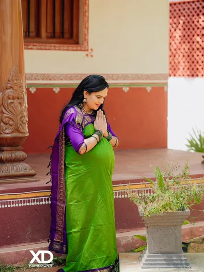 A respectful and serene pose of the mother-to-be in a traditional setting, with hands in a prayer-like gesture.