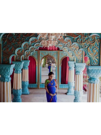 A stunning solo portrait of an expecting mother in a blue saree, standing in our vibrant Jaipuri palace set.