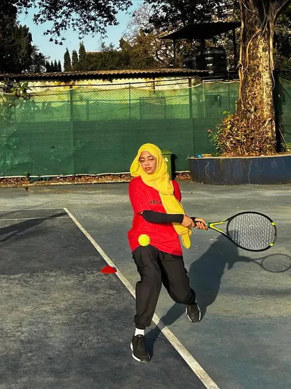 A player in a hijab and our team jersey executes a forehand, showing her focus and dedication during a drill.