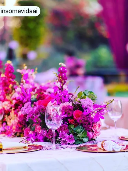 A close-up of the beautiful floral centerpiece and table setting at a Mehendi. The gold-rimmed plates and elegant wine glasses tie the whole look together.