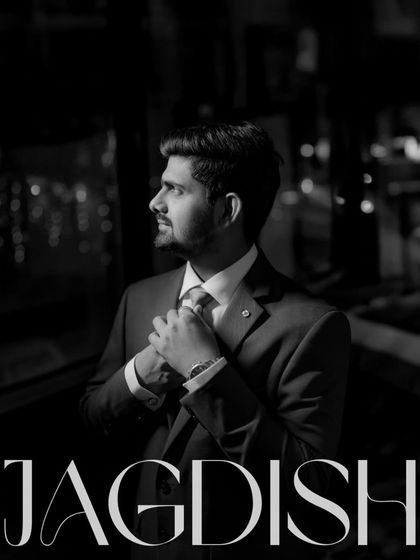 A dapper black and white portrait of the groom, Jagdish, adjusting his tie. This shot captures his suave and confident look for the reception.