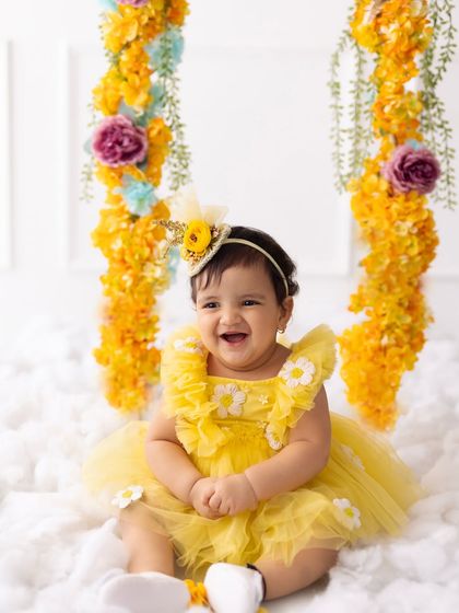A big, happy smile from the birthday girl on her floral swing. This shot captures the pure happiness of her first birthday celebration.