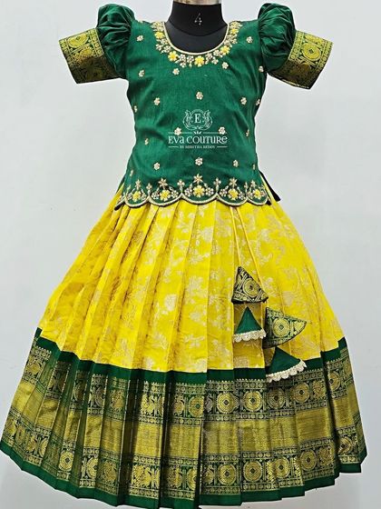 A traditional green and yellow Pattu Pavadai. The blouse has delicate floral embroidery, and the skirt has a rich green and gold border.