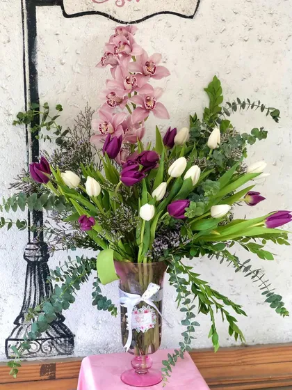This elegant vase arrangement showcases a beautiful combination of textures and colors. I've paired delicate pink orchids with bold purple and white tulips, accented with fresh eucalyptus leaves for a modern and sophisticated look that feels both fresh and timeless.