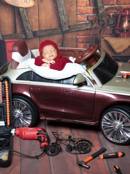 Another shot of our future mechanic, peacefully sleeping in his car. The composition highlights the contrast between the tiny baby and the rugged garage props.