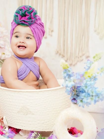 A happy baby girl surrounded by purple and blue flowers in her bath session. We love creating these colorful and joyful scenes.