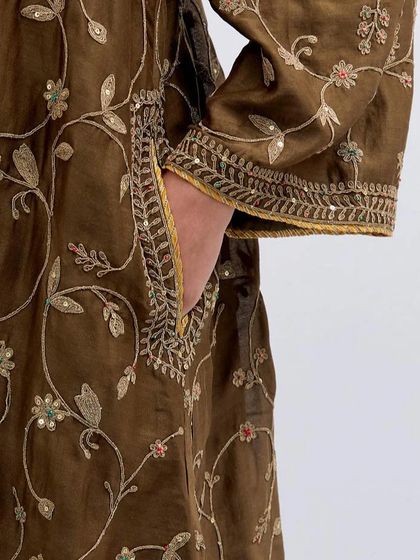 Embroidery that speaks the language of grace. A detailed shot of the sleeve and pocket of an earthy brown kurta, covered in delicate floral vine embroidery.