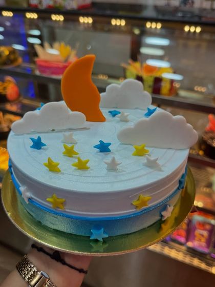 A dreamy cloud and moon theme cake. The soft blue and white colors, along with fondant stars and a crescent moon, create a peaceful and sweet design for a baby's celebration.