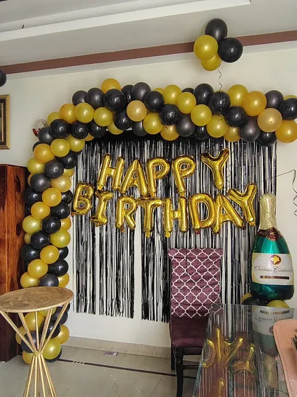 A classic black and gold birthday arch setup at home. This decoration includes a balloon arch, a black shimmer curtain, and a champagne bottle foil balloon for a touch of celebration.