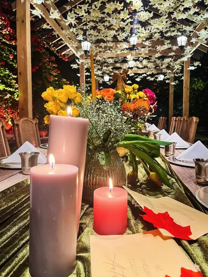 A close-up of the autumn tablescape, with glowing candles and personalized notes for guests. The ceiling above is adorned with hanging white leaves, adding to the magical fall setting.