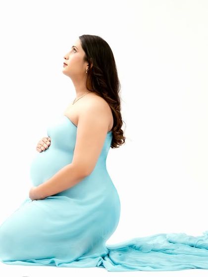 A simple and graceful profile shot. The mom-to-be looks upward, her form elegantly captured in a light blue gown against a pure white backdrop.