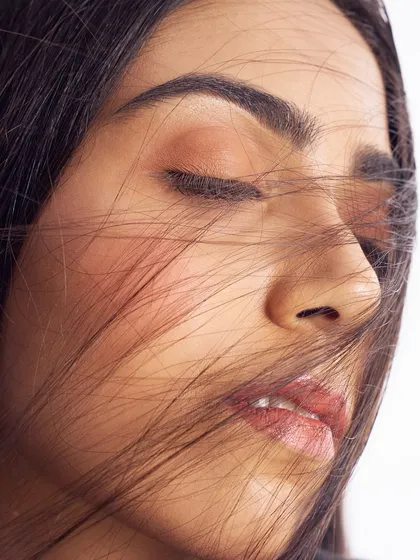 A soft, dreamy close-up. The wind-swept hair across the face adds a layer of texture, but the focus remains on the fresh, glowing skin and the simple, effortless beauty.