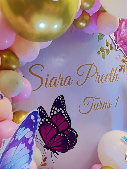 A close-up of a butterfly-themed first birthday backdrop. The soft pink and gold color palette and delicate butterfly graphics create a sweet and elegant look.