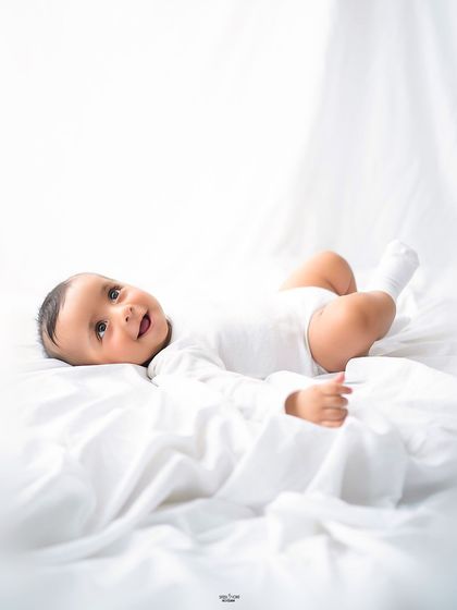 A happy baby enjoying his half-birthday session, lying on a soft white blanket.