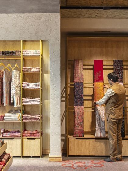 The display systems at Ahujasons are designed for both beauty and function. Here, a customer interacts with shawls hung on a vertical display, allowing the full pattern and texture of the fabric to be appreciated.