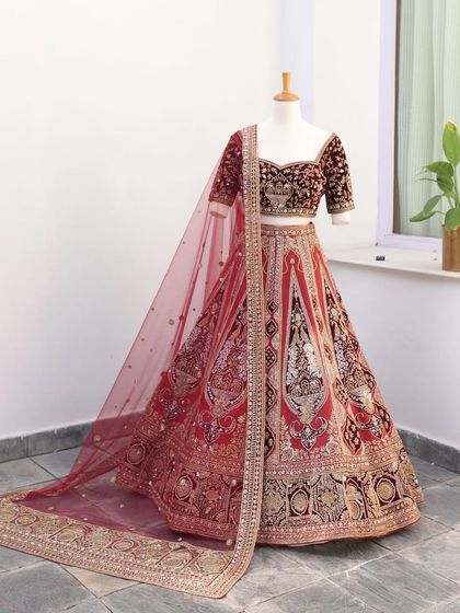 A classic red velvet bridal lehenga with heavy gold embroidery, displayed on a mannequin. This is a timeless piece that exudes royalty.