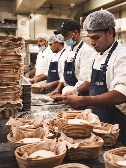 Our team of bakers works in unison, shaping and placing dough into baskets. It's a coordinated effort to produce hundreds of fresh loaves and pizza bases daily.