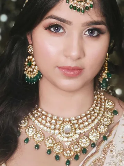 A classic and elegant look featuring a multi-layered Kundan necklace with green bead drops, paired with a white and gold outfit.