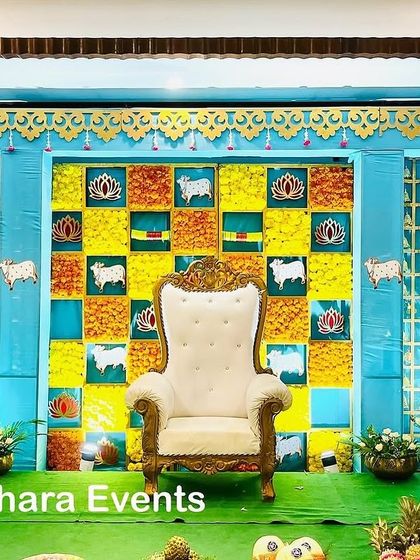 A vibrant Seemantham stage with a blue and yellow color scheme. The checkerboard backdrop is decorated with cow and lotus motifs, creating a cheerful and traditional atmosphere.