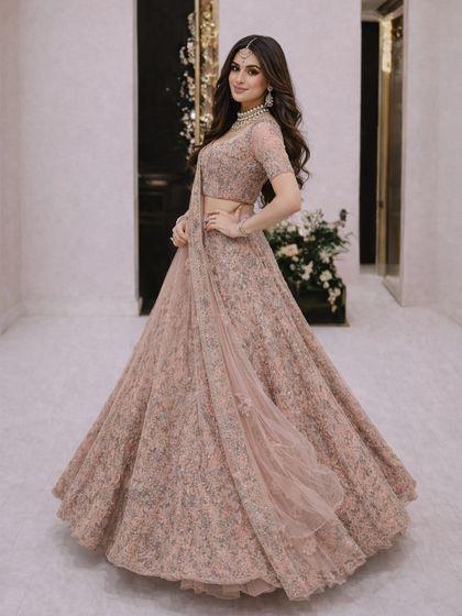 This pose showcases the flattering silhouette of the dusty pink lehenga, with its fitted blouse and voluminous, flowing skirt.