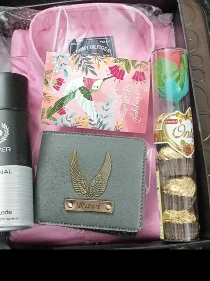 A birthday hamper filled with joy, featuring a personalized wallet, a pink shirt, a birthday card, deodorant, and chocolates.