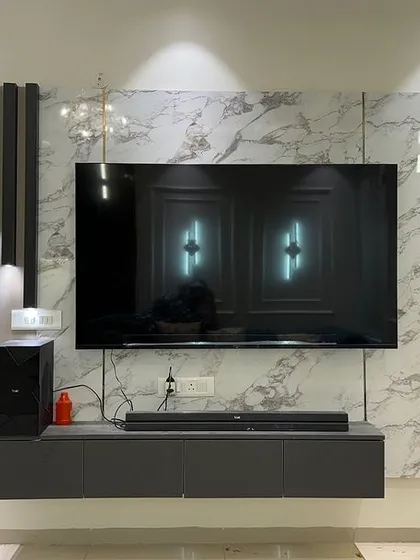 A floating TV unit in dark grey, set against a marble-finish wall. The open kitchen in the background shows a cohesive design language.